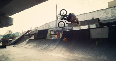 Milenyum çocuğu şehir kaykay parkında BMX bisikleti üzerinde takla atıyor. Sıradan bir erkek sporcu dışarıda bisiklet egzersizi yapıyor. Aktif motorcu şehir kaykay parkında ekstrem spordan hoşlanıyor. Spor konsepti.