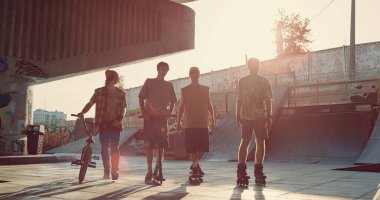 Genç arkadaşlar kaykaycı bmx binicisi kaykaycı ve scooter sürücüsü şehir kaykay parkında birlikte yürüyorlar. Erkek sürücüler günışığı şehrinde aktif olarak vakit geçiriyorlar. Gençlik kültürü spor konsepti.