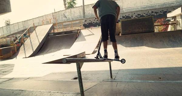 Active boy showing dangerous jump tricks on scooter at skatepark. Close up casual male rider in sneakers flipping scooter outdoors. Young man performing rail stunt at urban skate park. Sport concept.