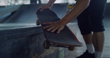 Kaykaycı kaykay pistinde elinde kaykayla geziyor. Yakından tanınmayan kaykaylı adam elleri. Kaykay parkında kimliği belirsiz bir adam var. Gençlik yaşam tarzı aktif eğlence konsepti. 