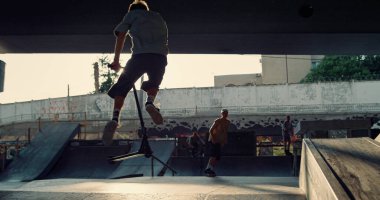 Günbatımında, kaykaylı patenle tehlikeli bir oyun antrenmanı yapan arkadaşlar BMX bisikleti kullanıyor. Aktif insanlar kaykay parkında vakit geçiriyorlar. Ekstrem spor gençliği kültür yaşam tarzı konsepti. 