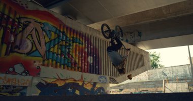 Kentsel kaykay parkında BMX bisikleti üzerinde enerjik çocuk eğitim yetenekleri. Dışarıda takla atan havalı bir motorcu. Dışarıda serbest stil yarışmasına hazırlanan ekstrem erkek binici. Sağlıklı yaşam tarzı gençlik kültürü kavramı.