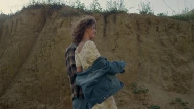 Smiling lovely couple walking beautiful nature near sand hills sunny morning. Happy carefree pair going on ocean beach together. Attractive curly girl have fun with stylish young guy outdoors.