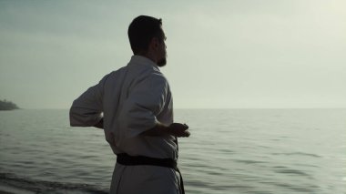 Gün batımında deniz kıyısında dövüş tekniğini mükemmelleştiren karate savaşçısı. Sakin atletik adam yaz akşamı kumsalda tekvando çalışıyor. Kimliği belirsiz sporcu dışarıda el egzersizi yapıyor..