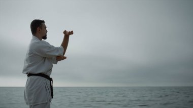 Sakallı sporcu sahilde kasvetli bir sabahta dövüş sanatları yapıyor. Kafkasyalı bir adam dışarıda karate öğreniyor. Deniz kıyısında dayanıklılık eğitimi veren ciddi bir sporcu. Spor etkinliği kavramı.
