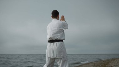 Bilinmeyen karate dövüşçüleri gündüz bulutlu havada saldırı talimi yapıyorlar. Aktif adam bulutlu gökyüzüne karşı deniz kenarında kumlu sahilde egzersiz yapıyor. Gün ışığında deniz kıyısında tanınmayan bir adam antrenman yapıyor..