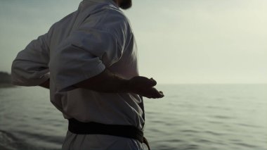 Bilinmeyen karateci elleri gün batımında savaş egzersizleri yapıyor. Dışarıda kimonoyla dövüş sanatları pratiği yapan sporcu. Sahilde kas sporcusu eğitimi, güzel manzaranın tadını çıkarıyor. Spor hayatı..