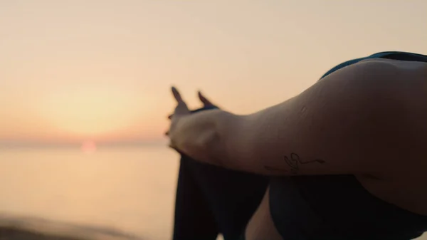 Unknown girl standing one leg holding knee at sunset outdoors. Athlete woman stretching body on beautiful beach. Unrecognizable slim sportswoman training balance doing sport exercise summer day.