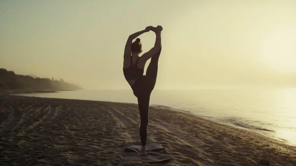 身材苗条的女孩练习分裂瑜伽姿势 一只腿在室外站得很近 柔韧的女运动员在夏日的海滨伸展身体 在柔和夕阳西下做体操的女运动员 — 图库照片
