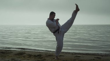 Kumsalda aktif tekme pratiği yapan bir atlet. Sakallı sporcu gün doğumunda dışarıda dövüş egzersizleri yapıyor. Güçlü adam yaz akşamları dışarıda dövüş eğitimi veriyor. Spor yaşam tarzı