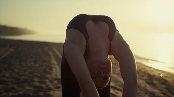 瑜伽女子弯腰地面照明日落阳光近身室外 美丽的女孩穿着深色运动服伸展身体 运动女子在海滨站着锻炼 — 图库照片