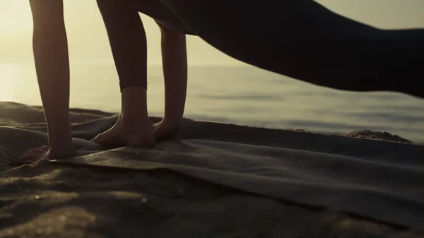 Sporty woman feet exercising standing sand seacoast at sunrise close up. Unknown barefoot girl practicing yoga on beach early morning. Flexible sportswoman stretching legs making gymnastic exercises.