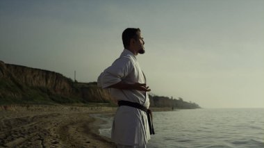 Vahşi bir sporcu kumlu sahil yaz akşamında meditasyon egzersizleri yapıyor. Karate dövüşçüsü gün batımında dövüş tekniğini mükemmelleştiriyor. Odaklanmış sporcu güneş ışığında dövüş sanatları çalışıyor..