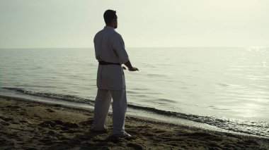 Sakin bir adam karate eğitimi alıyor sahilde gün batımını seyrediyor. Odaklanmış dövüşçü güneş ışığında dövüş sanatları yapıyor. Kum kıyısında duruyor. Vahşi sporcu kimono giyerek doğa üzerinde egzersiz yapıyor.