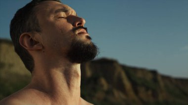 Vahşi sporcu, yaz sabahı doğa antremanında boynunu ısıtıyor. Sahilde uzanan düşünceli bir adam. Sakallı sporcu dışarıda egzersiz yapıyor. Sağlıklı spor vücut konsepti.