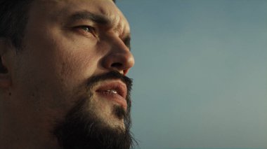 Akşam güneşini dört gözle bekleyen odaklanmış sakallı adamın portresi. Ciddi sporcu yüzünü kapat ve ağzını aç. Dışarıdaki su manzarasını izle. Orta yaşlı sporcu dışarıda dinleniyor, manzaranın tadını çıkarıyor.