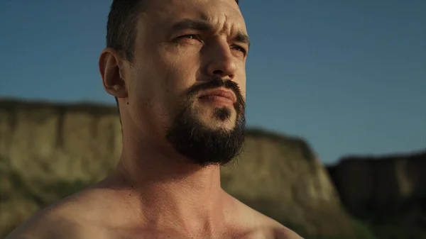 Closeup bearded karate man naked body warming up on seashore. Athletic sportsman exercising muscular hands on nature summer day. Brutal fighter stretching on sunlight standing beach. Sport lifestyle.