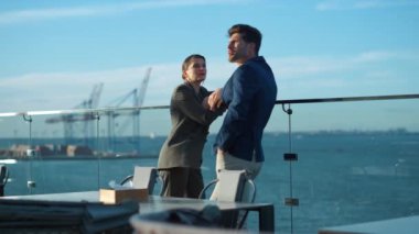 Financial managers discussing project on glass balcony in golden sunlight. Focused professionals business team talking commercial strategy rest at sea port view. Confident businessman investor concept