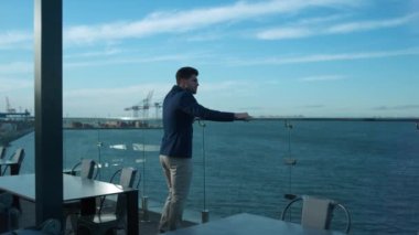 Successful man dreaming morning on luxury cafe balcony. Handsome freelancer rest enjoying sea view on lunch break alone. Confident businessman investor considering business problems on glass terrace.
