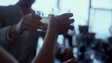 Couple hands clinking cocktails at luxury restaurant closeup. Unrecognizable lovers silhouettes celebrating anniversary and toasting alcohol beverages at romantic date in fancy cafe. Honeymoon concept