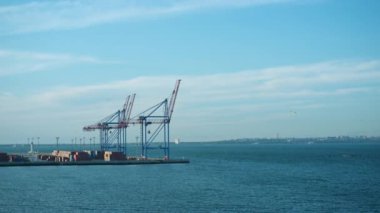 Sea port cargo terminal on calm sunny morning. Uploading cranes at cloudy sky. International container storage warehouse dock in ocean harbor. Metallic constructions at beautiful still water landscape