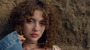 Şık güneş gözlüğü takan muhteşem kıvırcık kadın portresi. Kum tepesine yakın poz veren seksi çekici kız. Baştan çıkarıcı cazibe modeli kameraya özgüvenle bakıyor. Genç bayan doğada rahatlayın.