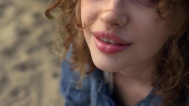 Beautiful girl face looking camera with happy smile close up. Portrait of cheerful attractive woman sitting sand beach alone. Seductive curly lady have fun relaxing on nature. Natural beauty concept.