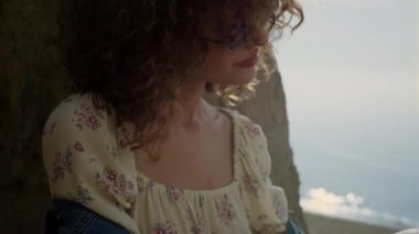 Güzel bir kadın sabah güneş ışığında kıvırcık saçlarını sallıyor. Deniz kıyısında güneşli bir günün tadını çıkaran çekici mutlu bir kızın portresi. Güneş gözlüklü genç bayan okyanus sahilinde rahatla. Doğa konsepti.