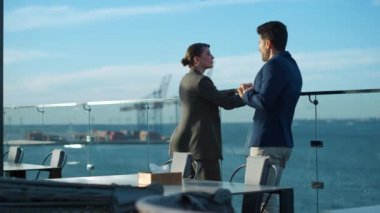 Business people talking outdoors in sunlight. Sales managers discussing project resting on glass terrace. Real estate professional showing cafe meeting client at sea view. Commercial deal concept.