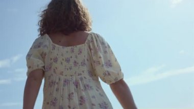 Sahilde dans eden kaygısız genç kız çiçekli elbiseler giyiyor. Mutlu, gülümseyen bir kadın hasır şapka takıyor ve yaz günü deniz kıyısını rahatlatıyor. Şirin kıvırcık bayan doğada iyi eğlenceler..