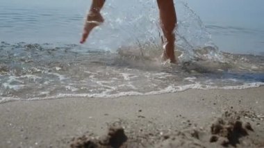 Bilinmeyen çıplak ayaklı kız su sıçratıyor okyanus dalgaları yaklaşıyor. Güzel ince bronzlaşmış bacaklar yaz günü ıslak deniz kumu üzerinde yürüyor. Mutlu, neşeli kadın deniz kıyısında rahatlarken sana iyi eğlenceler. Tatil kavramı.