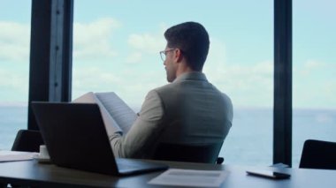 Yatırımcı deniz manzarasında sözleşme kağıtlarını okuyor. Düşünce yöneticisi panorama penceresindeki verileri analiz ediyor. Odaklanmış adam avukat finans belgelerini kontrol ediyor şirket raporlarını. İş adamı profesyonel. 