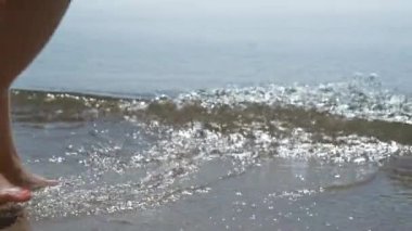 Güneş ışığında okyanus dalgaları saçan bronzlaşmış kadın bacakları. Sıcak deniz suyunda yürüyen bilinmeyen genç kızın çekici ayakları. İnce, rahat bayan turist deniz kenarında dinleniyor yaz tatilinin tadını çıkarıyor..