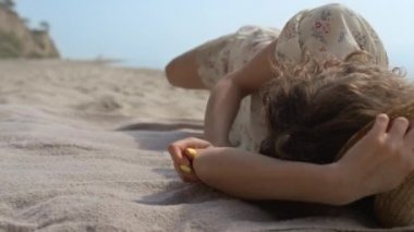 Gülümseyen kıvırcık kadın kumsalda yuvarlanırken iyi eğlenceler. Yaz tatilinde giysi giymiş, boş deniz kıyısında uzanan oyuncu bir kız. Neşeli bayan, güzel sahilde kaygısız olmanın keyfini çıkar..