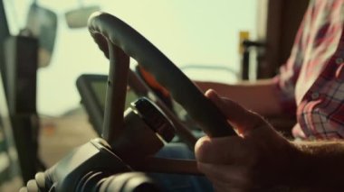 Sonbaharda tarımsal alanda direksiyonu elle kontrol eden sürücü yakın plan. Bilinmeyen traktör operatörü kontrollü hasat sürecini yönetiyor. Tarım işçisi otomatik hasat sistemini kontrol ediyor