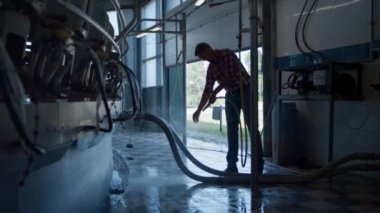 Farmer washing milking system in technological robotic farm using hose. Process of cleaning milk production equipment on modern automated cowshed. Computerized technology dairy producing concept.