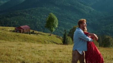 Genç aile yaz dağlarında birlikte dans ediyor. Güler yüzlü çift güneşli bir günde dışarıda eğlenir. Gülen aşıklar tatillerde kucaklaşırlar. Neşeli koca eşi turizm aktivitelerinde rahatlıyor. Aşk konsepti.