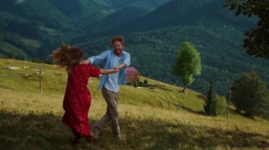 Neşeli çift dans dağları. Mutlu aşıklar doğa manzarasında el ele tutuşur. Aktif aile dışarıdaki yeşil arazide iyi eğlenceler. Dans eden genç insanlar yaz tatilinde tepeden aşağı koşuyorlar. Aşk konsepti