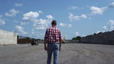 Agricultural business owner inspecting build process with backhoe loader outdoors. Man farmer walking on construction site for technical ranch. Quality control on building new big farm barn. 