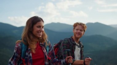 Laughing couple trekking mountains hike. Close up two tourists smile together outside on family vacation. Joyful backpackers enjoy walk in summer nature. Wanderlust happiness relationship concept.