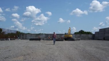 Construction inspector checking build process walking from yellow excavator outdoors. Professional builder controlling farm development stage in construction site. Inspecting building work concept.