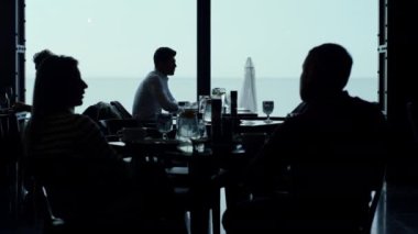 Stresli girişimci akşam yemeğini şık bir restoranda yiyor. Kafe misafirlerinin siluetleri panoramik barda dinleniyor. İş arkadaşları, karanlık otel salonunda öğle yemeği yiyor. Manzaralı deniz manzaralı bir yer.. 