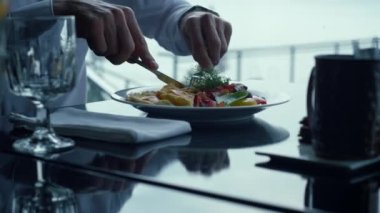 Unknown businessman cutting cooked food lunch bite. Elegant restaurant table setting close up. Male arms holding knife fork cutlery having tasty fresh breakfast closeup. Healthy diet concept.