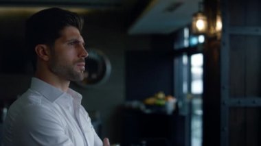 Charismatic businessman standing restaurant hall profile. Confident man resting lounge hotel bar. Elegant employee pondering business project in dark cafe. Scowling male face expression closeup.
