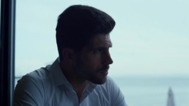 Çekici adam panoramik otel bar portresini rahatlatıyor. Güzel deniz manzaralı düşünceli bir adam restoran profilinde iş görüşmesi için bekliyor. Düşünceli erkek yüz ifadesi yakın plan.