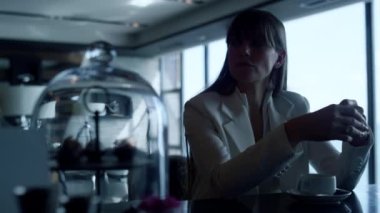 Closeup sad businesswoman drinking espresso alone. Upset woman portrait having coffee break at panoramic windows bar. Melancholic director sitting in dark restaurant interior. Loneliness concept