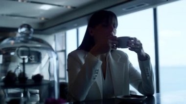 Closeup lonely woman drinking tea at restaurant. Depressed ceo thinking problems alone at panoramic windows view bar. Melancholic businesswoman portrait having aromatic coffee cup in dark interior