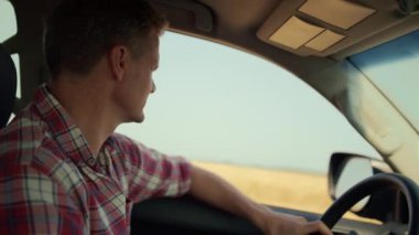 Man driving countryside inside vehicle closeup. Driver inspecting wheat field looking suv window on sunny day. Focused farmer observing harvested grain farmland. Agrarian enjoying crop meadow trip