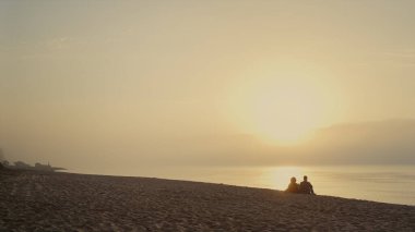 Sahilde gün batımını izleyen sevimli bir çift. Geniş açılı erkek arkadaş ve kız arkadaşın denizde buluşması. Arka plan dostları okyanus kıyısında birlikte dinleniyorlar. Gün doğumunda deniz manzarası. Boş zaman konsepti