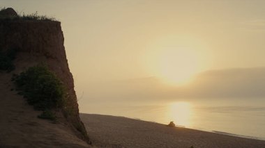 Gün doğumunda kumlu sahilde oturan geniş açılı romantik çift. Dostlar deniz kıyısında kucaklaşıyorlar. Sevgi dolu kadın ve erkek gün batımının tadını çıkarıyor. Güneş ışıkları okyanus yüzeyine düşüyor. Seyahat kavramı